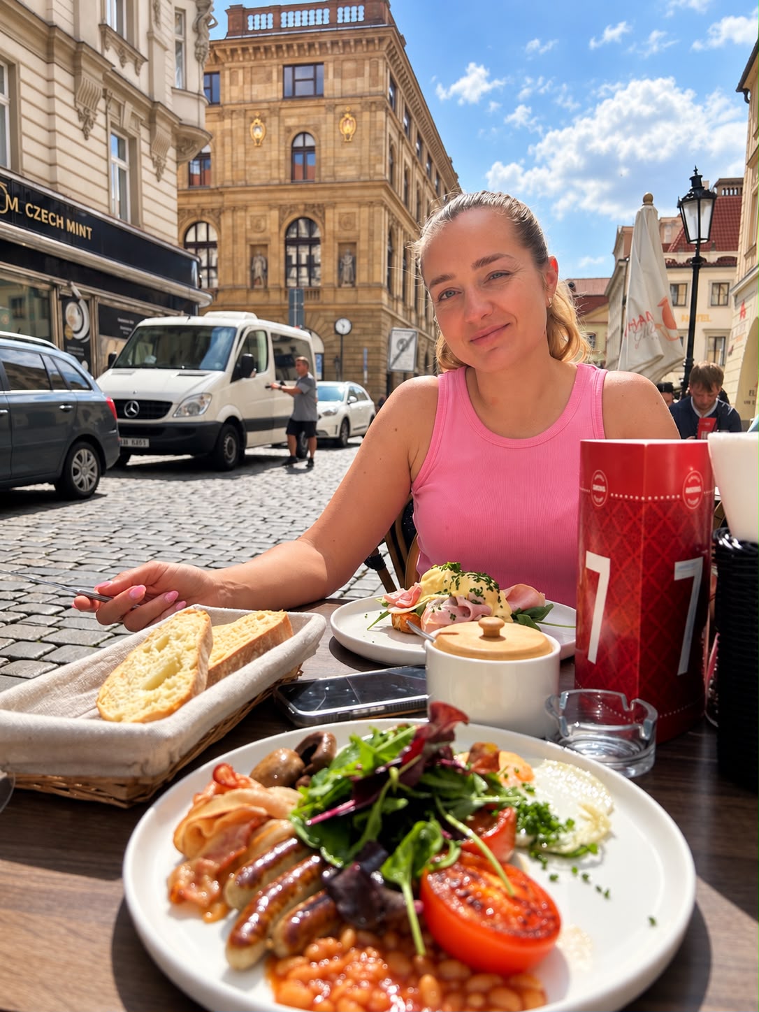 Monika na raňajkách pri stolíku na ulici, pred ňou veľký tanier